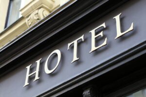 Close-up of a black sign with large, gold-colored letters spelling "HOTEL" mounted on a stone building.